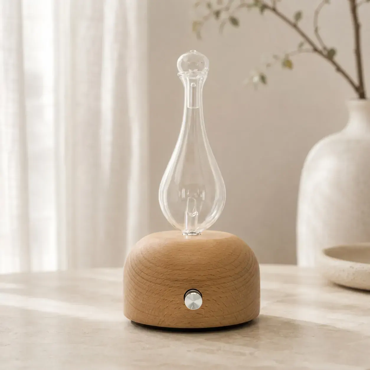 Dual-Fluid Aroma Diffuser — pear glass on wood dome Pear-shaped glass dual-fluid aroma diffuser on a light wood dome base
