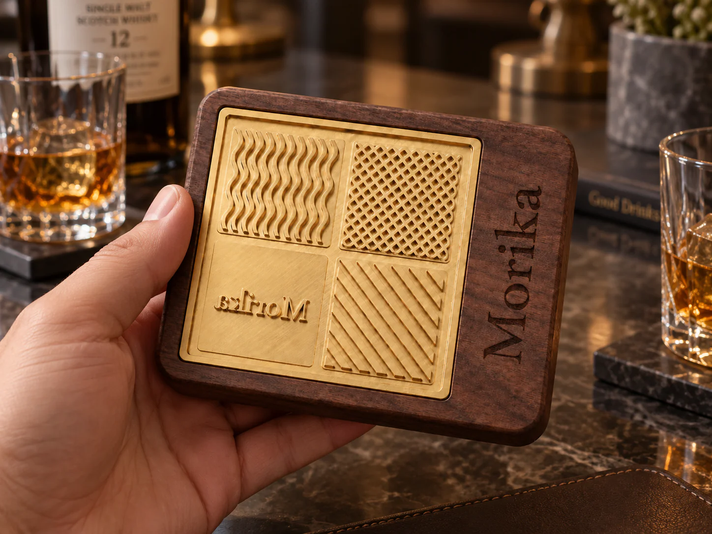 Hand holding a copper and walnut ice branding stamp on a bar beside whiskey glasses Hand holding a copper and walnut ice branding stamp on a bar beside whiskey glasses